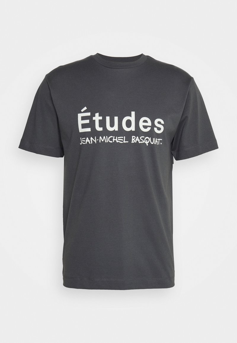 T-shirt en coton gris foncé avec un texte blanc audacieux qui indique "Études" et "JEAN-MICHEL BASQUIAT." Col rond classique et manches courtes.