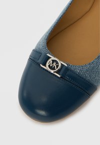 Bailarina azul marino con puntera de cuero lisa, parte superior de tela tipo mezclilla y un adorno decorativo plateado con el logo MK.