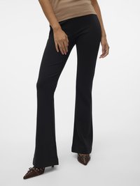 Melni platie bikses, izgatavotas no gludas auduma, ar pieguļošu vidukli un elegantu siluetu, apvienotas ar brūnām kurpēm ar norādītu purngali.