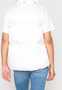 Biała kamizelka puchowa na krótki rękaw z wysokim kołnierzem, zamkiem błyskawicznym i lekko ściągniętym elastycznym pasem. Gładki, błyszczący materiał.