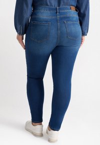 Jeans ajustados de mezclilla azul oscuro con una textura suave, que cuentan con dos bolsillos en la parte trasera y un diseño entallado que se ajusta en los tobillos.