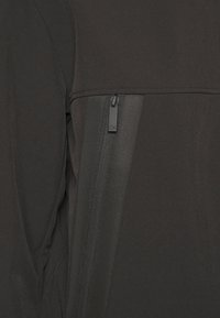 Giacca nera con zip in tessuto liscio, caratterizzata da un pannello a contrasto, dettagli conzip e un logo discreto sul tirazip.