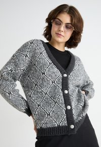 Grijze en zwarte gebreide cardigan met een V-hals, grote knopen en een gebreide textuur. Heeft een losse pasvorm en lange mouwen.