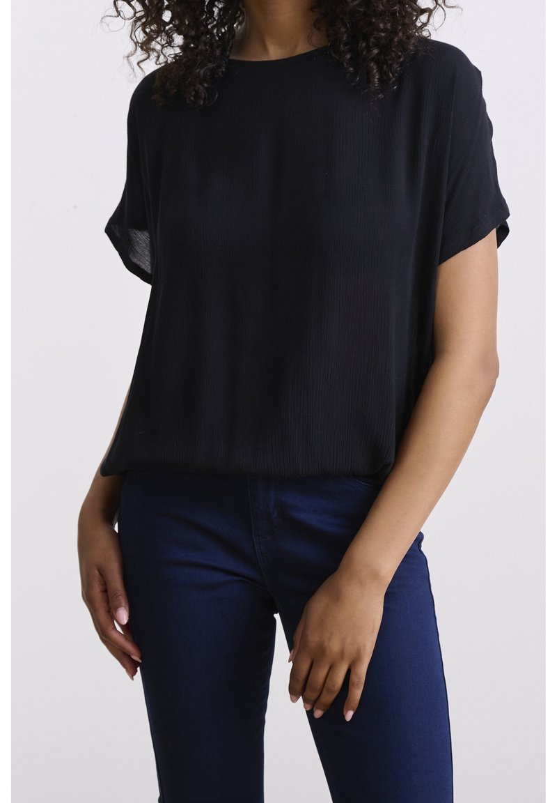 Haut noir à manches courtes avec une coupe décontractée et une texture côtelée, associé à un jean slim bleu foncé.