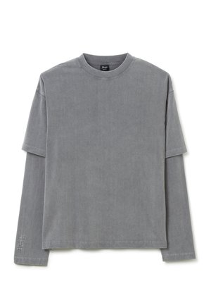 Camiseta de manga larga gris, de material de algodón suave, con cuello redondo, que presenta un sutil detalle cosido en la manga, de corte relajado.