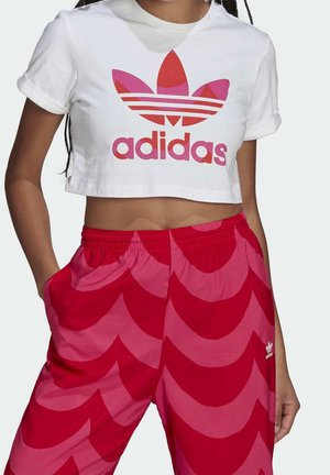 Witte cropped Adidas T-shirt met roze en rood logo, gecombineerd met rode en roze brede broek met patroon en zijzakken.
