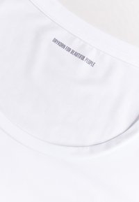 Bílá bavlněná tričko s širokým výstřihem a malou potištěnou cedulkou na zadní straně s textem "DRYKORN FOR BEAUTIFUL PEOPLE."