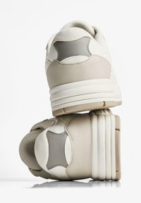 Masivne tenisice u krem i svijetlo sivoj boji. Teksturirane mrežaste i glatke kožne materijale, slojeviti naglasci i debele gumene potplate.
