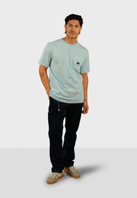 Lichtblauw, T-shirt met korte mouwen en een borstzakje met een klein olifantenlogo. Gepaard met zwarte broek en beige sneakers.
