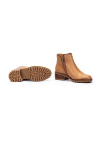 Bottines en cuir tan avec une fermeture éclair sur le côté, bout arrondi et petit talon carré. Semelle en caoutchouc texturé avec des motifs antidérapants.