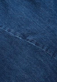 Tissu en denim bleu avec une couture diagonale visible et un motif de tissage texturé en gros plan.