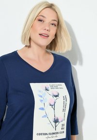 T-shirt in cotone blu navy con scollo a V e maniche corte, caratterizzato da una stampa grafica floreale in colori pastello e testo su uno sfondo chiaro.