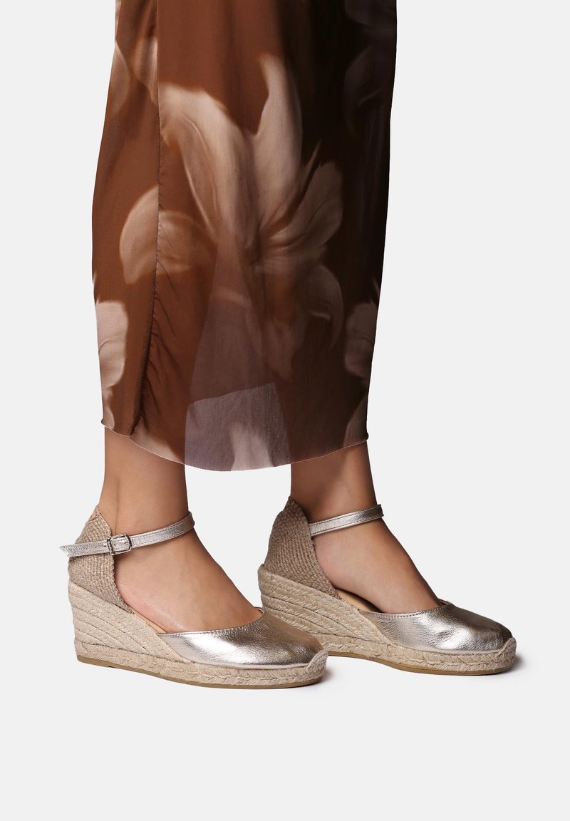 Metallic silver wedge sandals with ankle strap, featuring a woven jute base and smooth leather upper. Casual design with open sides.