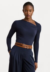 Marine lange mouwen top met een gedrapeerde halslijn, gecombineerd met hooggetailleerde broek en een bruine dubbelgespikte riem. Glad materiaal en gepaste pasvorm.
