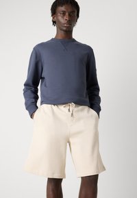 Navy blue sweatshirt with crew neck and long sleeves paired with beige, knee-length shorts featuring an elastic waistband and side pockets.