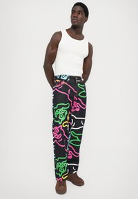 Black denim pants featuring colorful cartoon designs in pink, green, and blue, with a straight-leg cut and a waistband with buttons.