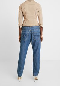 Beige denim jas met driekwartmouwen en een rafelige zoom, gecombineerd met losvallende blauwe jeans met twee achterzakken.