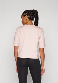 Camiseta cropped de manga curta rosa, feita de um tecido suave, com decote redondo e uma textura lisa, combinada com leggings pretas.