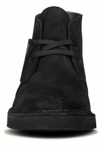 Black suede ankle boots feature a round toe, flat sole, and textured upper with black laces and a subtle embossed logo on the side.
