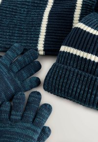 Marineblå strikkede handsker og hue med hvide striber. Handskerne har en struktureret stof; huen har et ribbet design og kontrasterende striber.