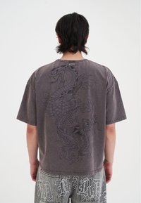 Oversized gray T-shirt with a black dragon graphic on the back. Features short sleeves, a round neckline, and soft fabric texture.