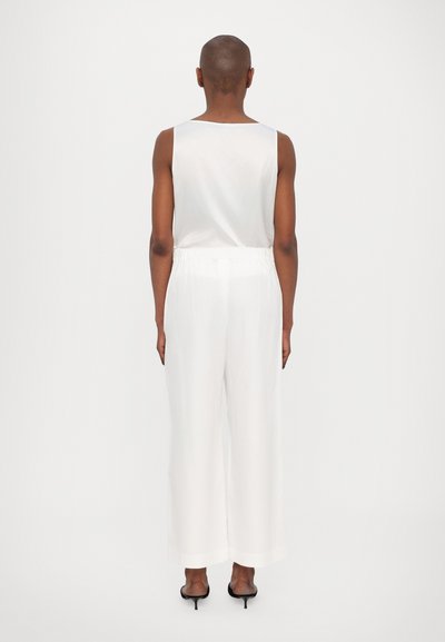 Valge, varrukateta top ümmarguste kaelusega, kokku sobitatud laia jalgadega valgete pükstega. Sile kangas, pükstel elastne vöökoht.