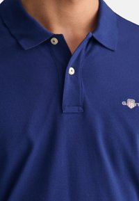 Blue polo shirt made of textured fabric, featuring a classic collar, two buttons, and a small logo on the left side.