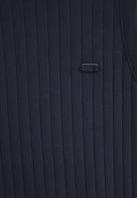 Tissu côtelé bleu marine foncé avec une petite étiquette en métal noir embossée de "POLO CLUB" attachée sur le côté droit.