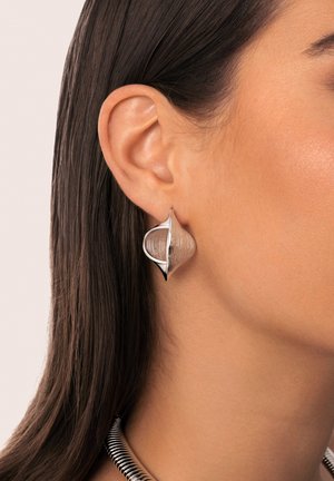 Los pendientes de plata presentan un diseño abierto en espiral con una superficie texturizada y acentos pulidos. Se llevan en una oreja, mostrando su forma única.