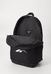 Zwarte rugzak met een rits hoofdcompartiment, voorzien van een mesh zijzak en een wit Reebok-logo aan de voorkant. Duurzaam materiaal en een strak ontwerp.