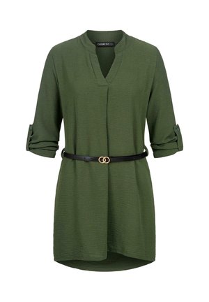 Vihreä pitkähiha tunika, jossa käärityt hihat ja musta vyö, jossa kaksoisrenkainen kultainen solki vyötäröllä.