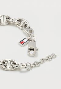 Ασημένιο βραχιόλι αλυσίδας με οβάλ κρίκους, με κούμπωμα και ένα μικρό ορθογώνιο φυλαχτό με κόκκινες, λευκές και μπλε ρίγες σε λευκό φόντο.