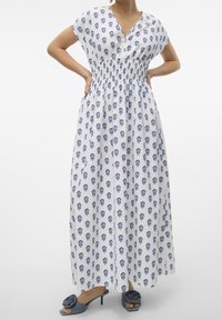 Weißes Maxikleid mit blauem Blumenmuster, kurzen Ärmeln und gerafftem Taillenbereich. Kombiniert mit blauen Rutsch-Sandalen mit Blumenverzierungen.