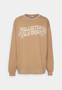 Felpa color crema con grafica "HOLLISTER CALIFORNIA" in bianco. Polsini e orlo a costine, scollo rotondo e vestibilità comoda. Morbido tessuto in misto cotone.