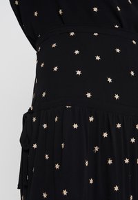 Abito nero con ricamo di stelle dorate, vita arricciata e dettaglio con fiocco laterale. Tessuto morbido con una consistenza liscia, adatto per un abbigliamento casual.