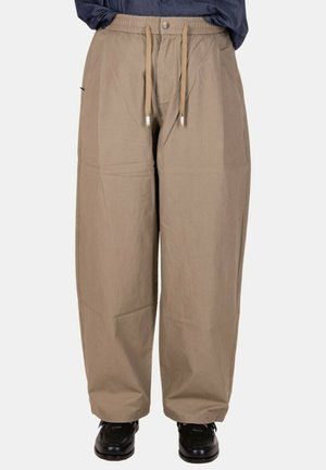Pantaloni beige a vestibilità ampia con vita elasticizzata e coulisse, indossati con scarpe nere e camicia blu scuro infilata.