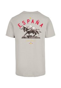 Világosszürke póló, amelyen egy bika és egy focilabda látható, piros színű "ESPAÑA" felirattal és arany színű "¡A por ellos!" felirattal alatta.