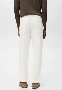 Pantalons en lin blancs avec une coupe décontractée et deux poches arrière, associés à une chemise marron à manches courtes côtelée et des chaussures en daim marron.