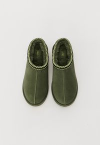 Chaussons en suède verts à enfiler, avec doublure en shearling, zigzag contrasté le long du bord supérieur, et semelle en caoutchouc plate.