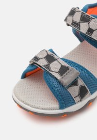 Blå och grå sandal med meshupp överdel, hexagonal mönsterremmar, stoppad sula och orangea detaljer på sulan.