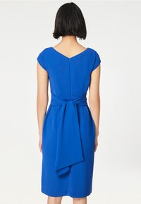 Blå klänning med korta ärmar, figurnära passform, knälång. Har en dragkedja i ryggen och en knytning i midjan, slätt tyg.