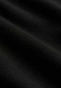 Černá tkanina s hladkým povrchem, ukazující jemně pletené vazby a mírný lesk. Materiál vypadá měkce a pružně.