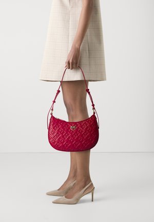 Borsa a tracolla rossa trapuntata con motivo in rilievo, dettagli in oro e tracolla regolabile, tenuta da un modello in un vestito a quadri e tacchi color nudo.