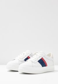 Białe sneakersy z gładkiej skóry, z niebieskim i czerwonym paskiem po bokach oraz białą gumową podeszwą.