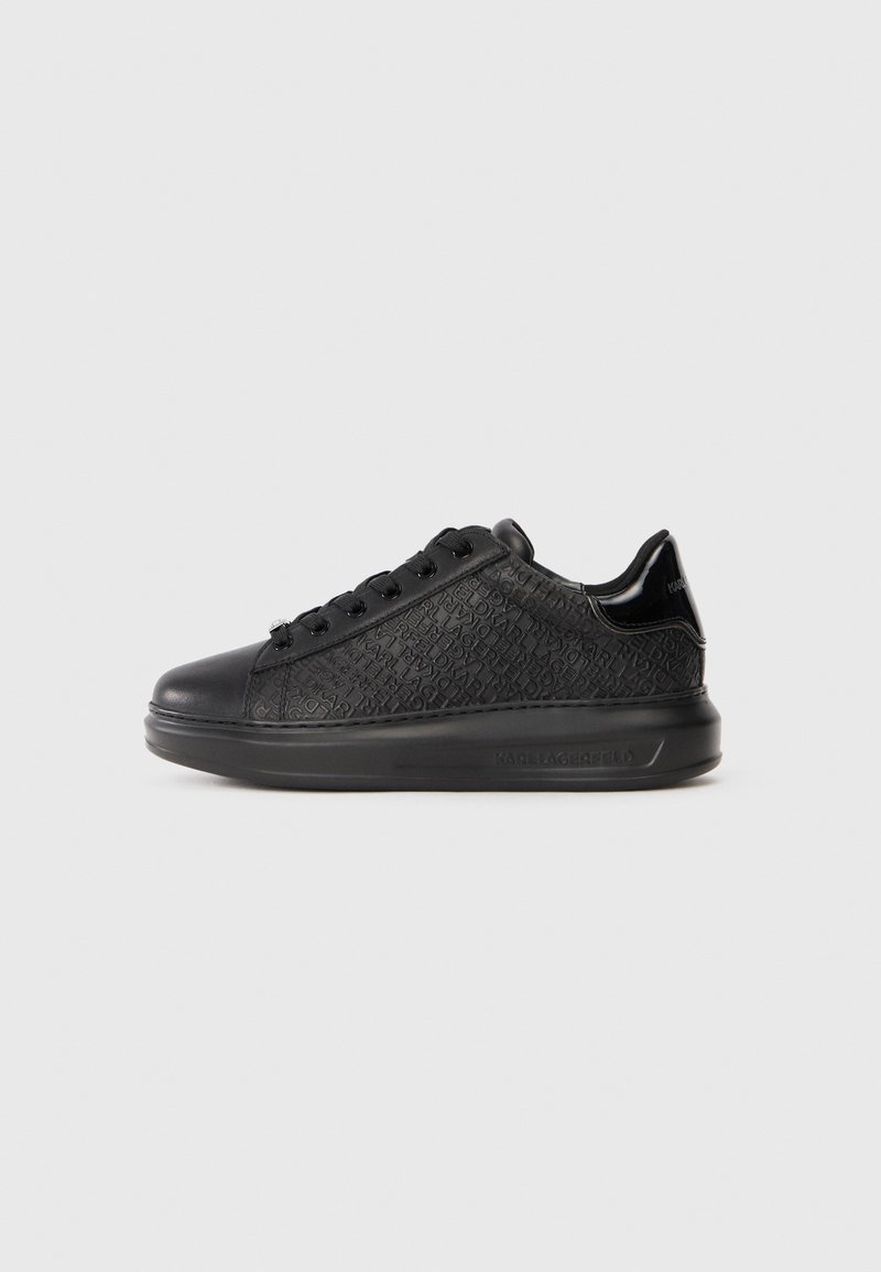 Schwarze Sneakers mit einer strukturierten Oberseite, die ein wiederkehrendes Logomuster zeigt, flacher Schnürverschluss und eine robuste Gummisohle.