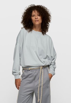 Hellblaues, übergroßes Sweatshirt mit gerippten Bündchen und Rundhalsausschnitt, kombiniert mit grauen Jogginghosen mit Kordelzug und seitlichen Akzenten.