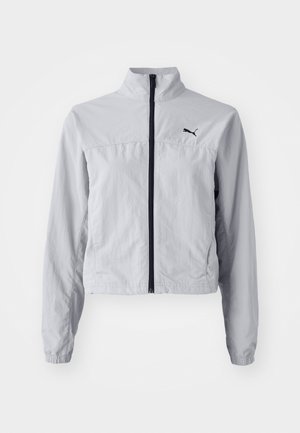 Lichtgrijze windbreaker jas met een hoge kraag, volledige rits aan de voorkant en elastische cuffs. Bevat een zwart logo op de bovenste linkerkant.
