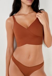 Bralette in tessuto elastico marrone con scollatura a V e design frontale incrociato. Spalline regolabili e bikini coordinato a coste.