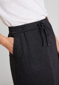 Pantalon de jogging noir en tissu texturé, avec taille élastique, cordon de serrage et poches latérales. Vue rapprochée montrant les détails et l'ajustement.