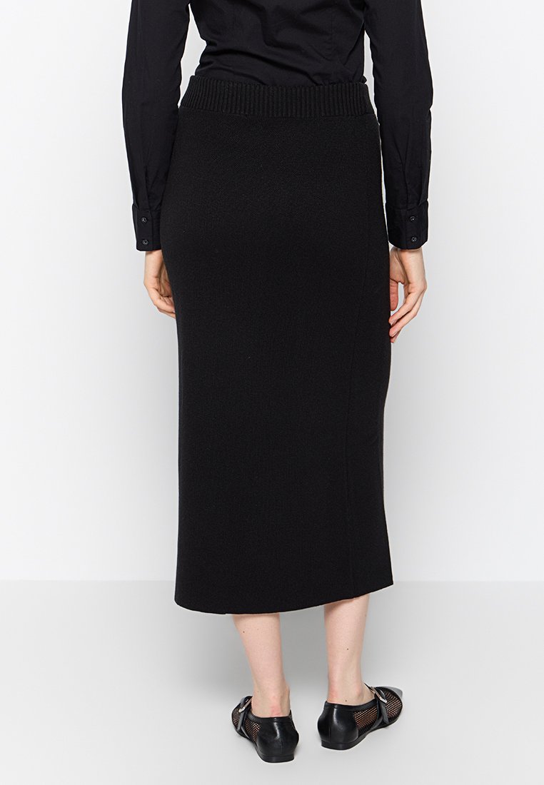 Falda midi negra de punto con una cinturilla acanalada, que presenta una silueta recta y una textura suave, combinada con zapatos de malla negros.